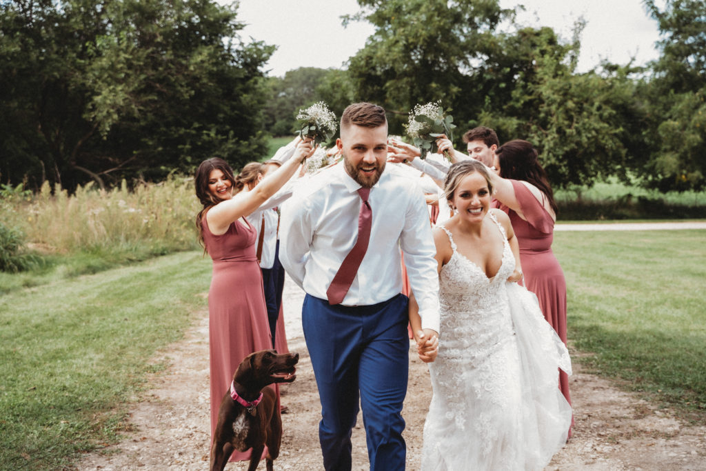 bride and groom run through wedding party tunnel with dog